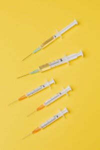 Top view arrangement of medical single use syringes with vaccine and small empty syringes without needle cover placed on yellow surface