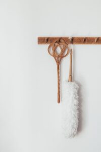 Soft dust brush and fly swatter hanging on wooden hanger on white wall