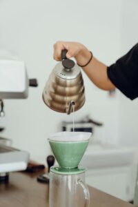 Unrecognizable female barista preparing delicious coffee in glass coffeemaker and pouring hot water during at table in modern cafeteria