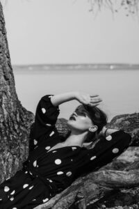 Woman in Black and White Polka Dot Dress Leaning on Brown Tree Trunk