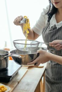 Crop females draining cooked homemade pasta