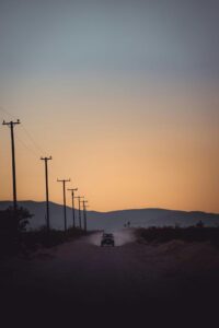 View of a Car on a Dirt Road with Silhouetted Mountains in Distance at Sunset