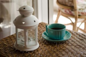 White Candle Lantern Beside of Blue Ceramic Coffee Mug on Wicker Table