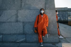 Man in Orange Coat Standing Beside Gray Concrete Wall